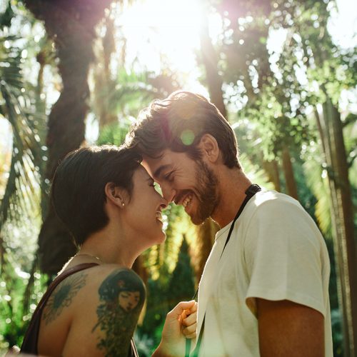 Man and woman standing close touching their noses in a park with sun in the background. Tourist couple in a happy and romantic mood while exploring the city.